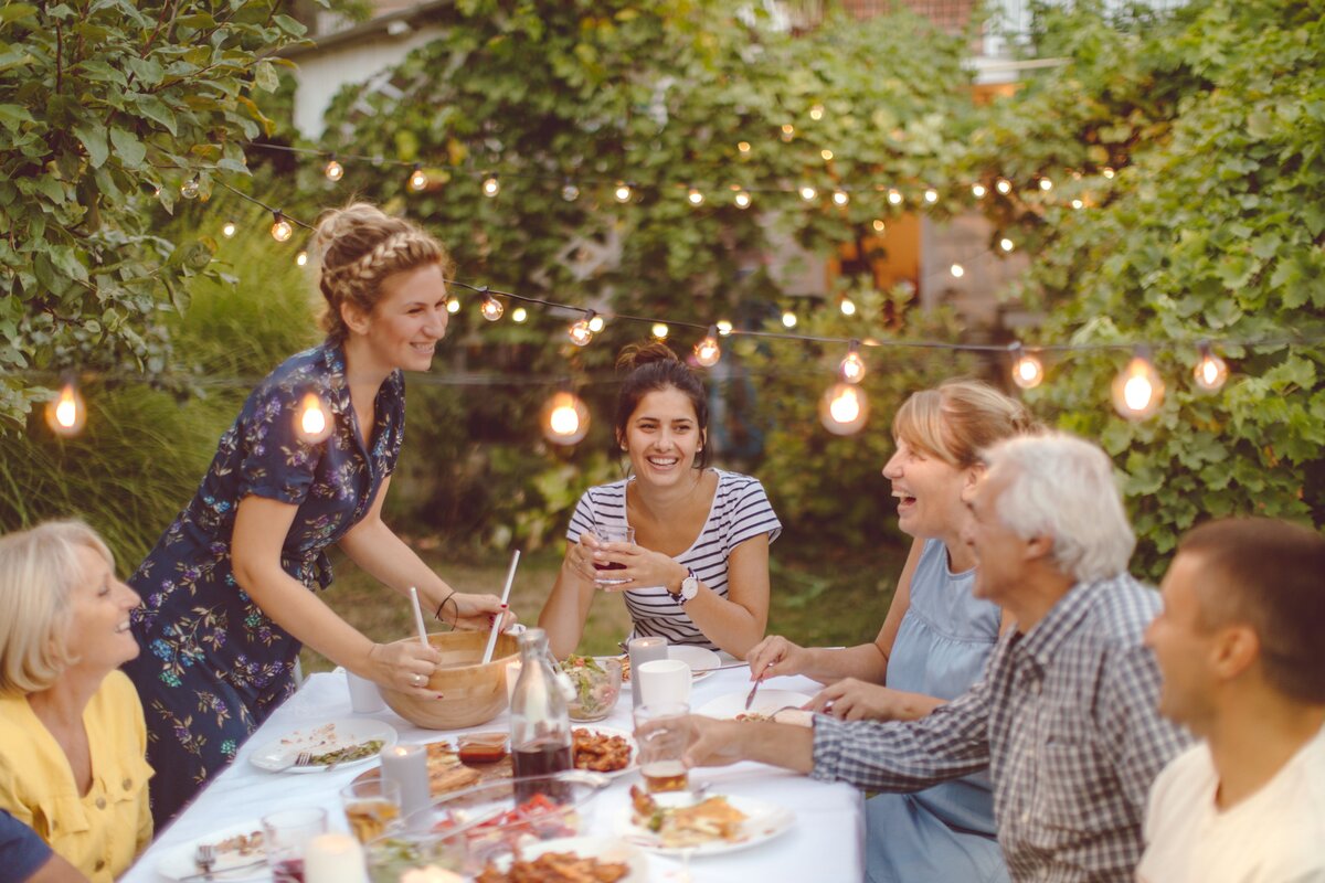6 people sit around a table outside laughing and eating