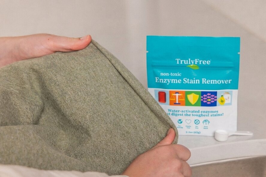 Shirt with chocolate stain removed and Truly Free Home Enzyme Stain Remover in the background. 