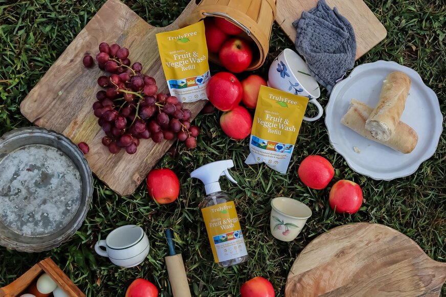 Apples, grapes, and bread in a picnic spread with Truly Free Home Fruit & Veggie Wash.