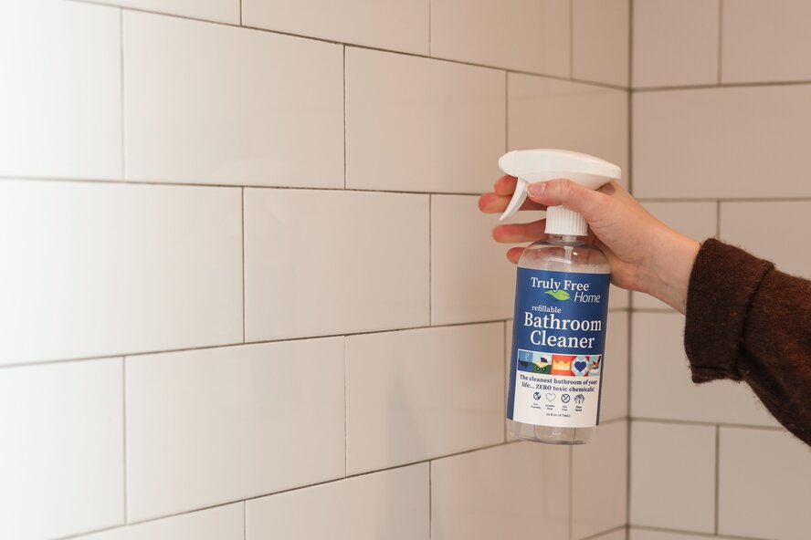 Spraying Truly Free Home Bathroom Cleaner on shower wall