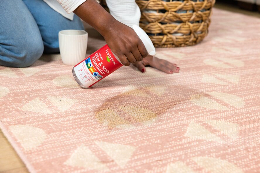 Woman using Truly Free Home Odor & Stain Eliminator to get a coffee stain out of a rug.