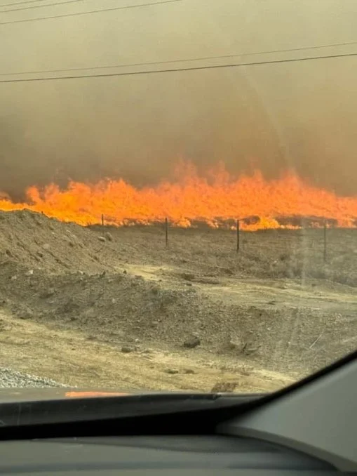 Grass fire along a dirt field edge seen through a windshield