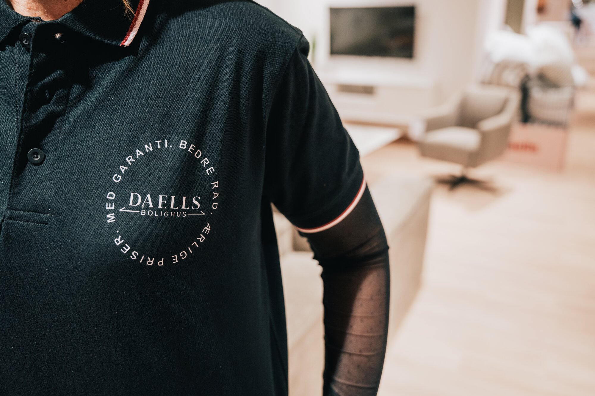 Close up af Daells Bolighus uniform med lyserødt logo på den sorte bluse.