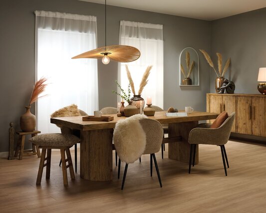 Spisestue indrettet i boho stil med stort massivt spisebord i fyrretræ. Omkring det er stole i beige boucle, stor skænk og interiør i boho stil.