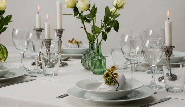 Elegant borddækning med hvid dug, sølvlysestager, grønne vaser og hvide roser – klassisk og stilfuldt festbord fra Daells Bolighus.