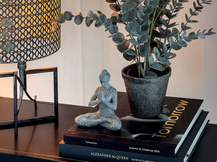Indretningstrenden at indrette med personlig stil, som afspejler dig. Her er der indrettet med en bordlampe, yoga figur, plante og bøger.