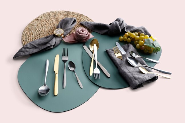“Bestik og stofservietter i guld og sølv på grønne dækkeservietter – moderne og stilfuld borddækning med naturlige detaljer fra Daells Bolighus.