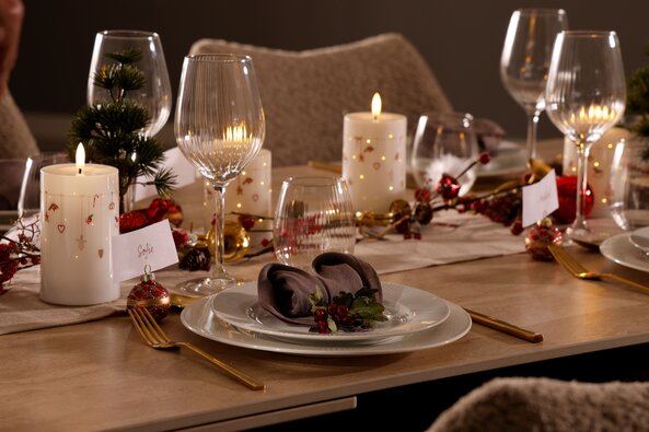 Julebord dækket med stearinlys, guld bestik, røde dekorationer og navnekort – hyggelig og elegant julestemning fra Daells Bolighus.