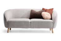 Lysegrå sofa med runde former omkring armlæn og med skrå egestræben. Pyntet med tre pyntepuder.