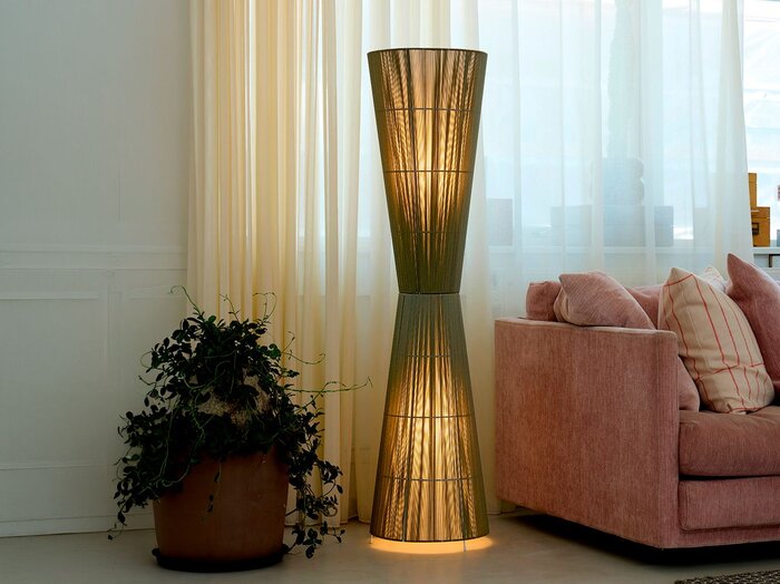 Dekorativ olivengrøn gulvlampe, som er en ad tidens trends. Står i dagligstue med lange gardiner, plante og rosa sofa.