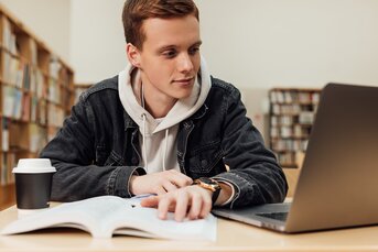 Ung mand studerer ved en bog og computer