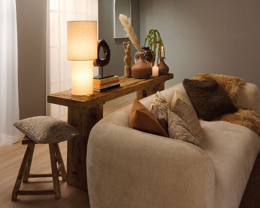 Boho indrettet stue med rustikt konsolbord bag ved sofaen pyntet med lampe, keramikvaser og figurer.