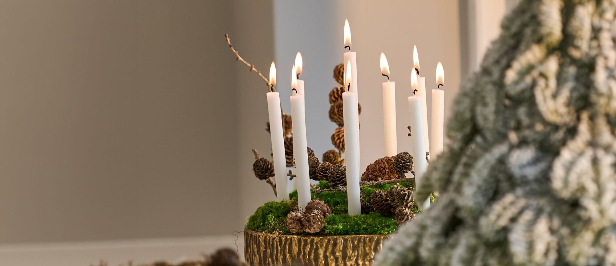 Stemningsfuldt julebord med julekrus med motiver, glaskrukker med pebernødder og juleskum, omringet af vaniljekranse, gran og en julemandslysestage.