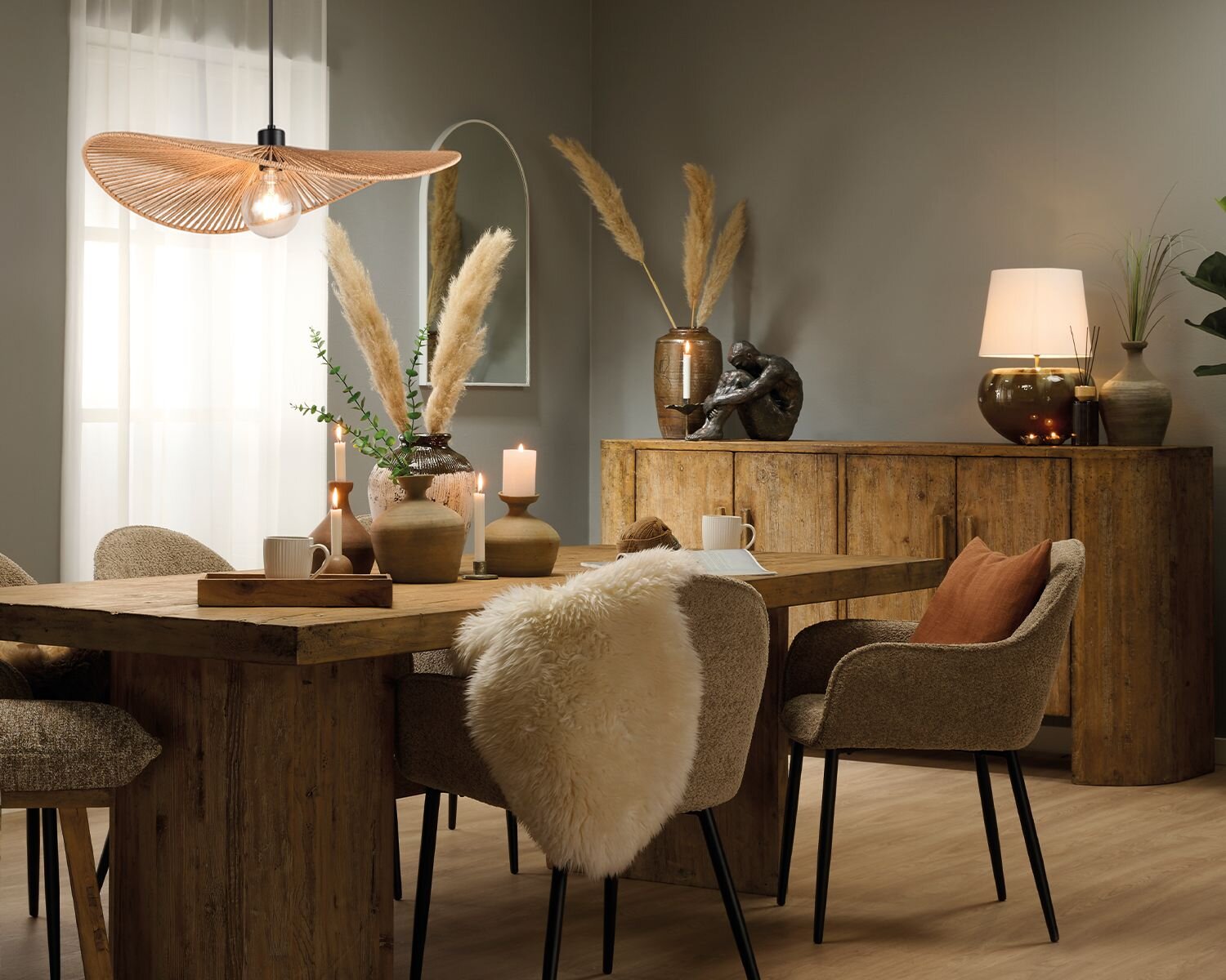 Spisestue indrettet i boho stil med rustikke træmøbler, planter, keramik vaser og jordfarver. I midten står et stort spisebord omringet af stole, og for enden af rummet står en stor massiv skænk.