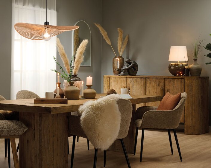 Spisestue indrettet i boho stil med rustikke træmøbler, planter, keramik vaser og jordfarver. I midten står et stort spisebord omringet af stole, og for enden af rummet står en stor massiv skænk.