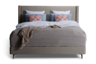 Polstret dobbeltseng med lys sengegavl, neutralt sengetæppe og farverige pyntepuder – elegant og indbydende soveværelsesindretning med fokus på komfort.