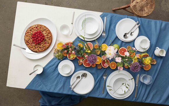 Farverigt dækket bord med hvidt stel, blå dug, friske blomster og citrusfrugter som bordpynt – inspiration til festlig borddækning fra Daells Bolighus.
