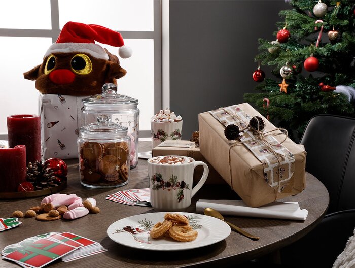 Hyggelig juleopdækning med småkager, varm kakao, gaver og julepynt ved siden af et juletræ.