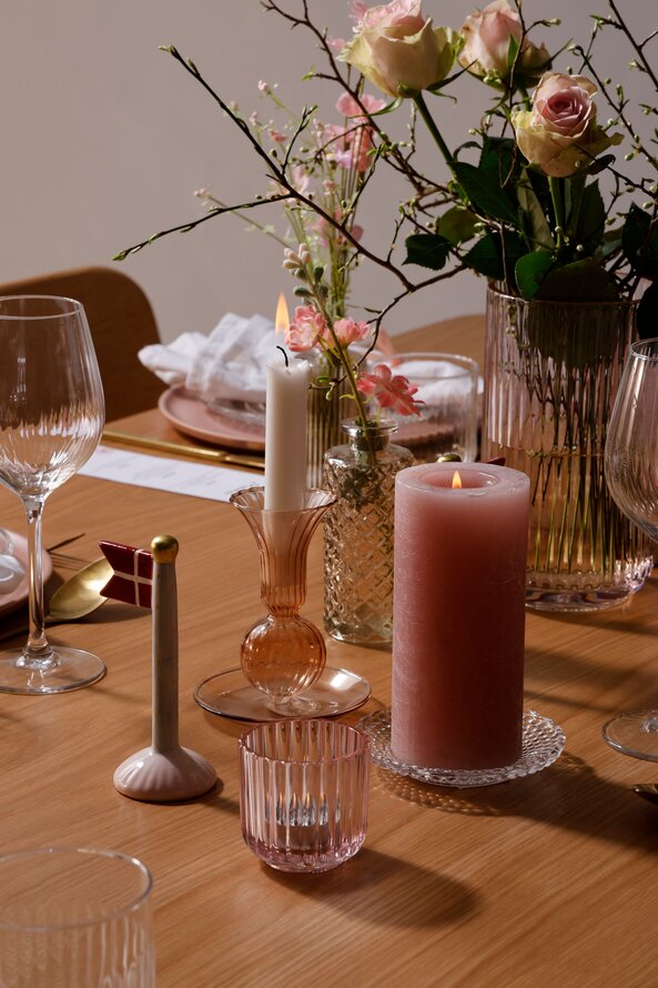 Detaljer på konfirmationsbord med keramikflag, rosa fyrfadsstage, orange lysestage, rosa bloklys på glastallerken, samt stor buket i rosa vase. Alt stillet på midten af bordet.