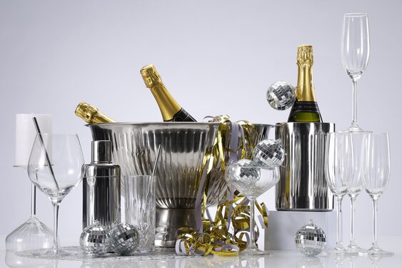 Nytårsting på et bord med drinksglas, champagneglas, cocktailshaker, vinkøler, champagnekøler og små diskokugler