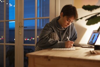 Ung studerende sidder ved skrivebord og skriver