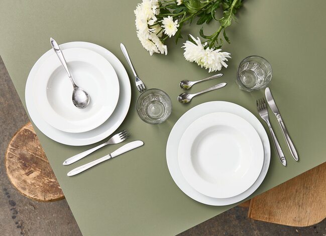Formel borddækning med hvidt stel, blankt bestik og friske hvide blomster på grøn dug – enkel og elegant bordopdækning fra Daells Bolighus.
