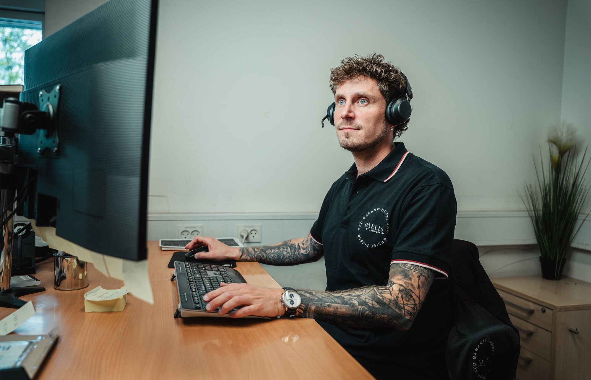 Mandlig kundeservice medarbejder sidder ved skrivebord med computer og tastatur med headset på.