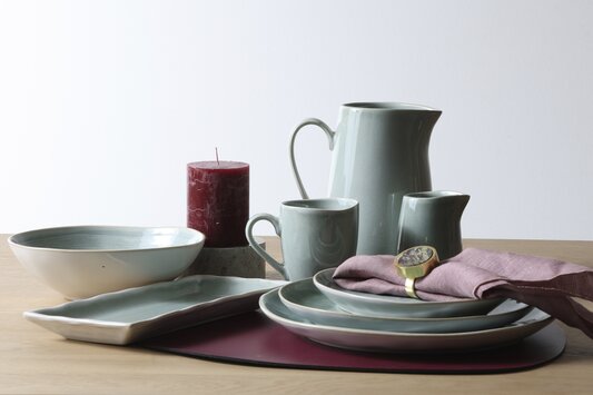 Dacore stentøjsstel opstillet i mintgrønt på lys træbordplade med en bordeaux dækkeservietter, bloklys og en rosa serviet med messing servietring
