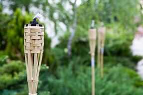 Bambusfakler står placeret i en grøn have med frodig beplantning og skaber en hyggelig og stemningsfuld udendørs atmosfære.