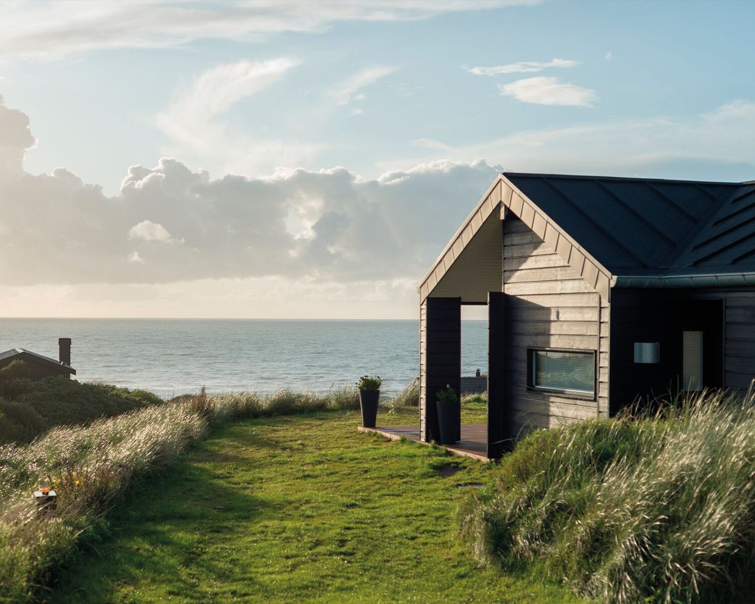 Sommerhus med havudsigt omgivet af klitgræs og natur tæt på stranden.