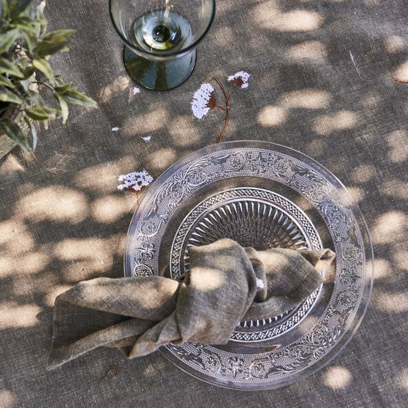 Glastallerken dækket op på en dug ude i haven med en stofserviet, der er bundet knude på, der er placeret på tallerken.