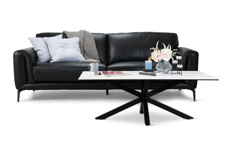 Violino Collection sort 3-personers lædersofa med slanke metalben, polstrede sæder og bløde ryghynder i moderne design. Sofaen er pyntet med blå puder og har et lyst sofabord foran.