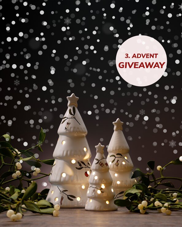 Tre dekorative porcelænsjuletræer med indbygget lys står på et bord omgivet af mistelten. I baggrunden ses snefnug på mørk baggrund samt teksten “3. advent giveaway”.