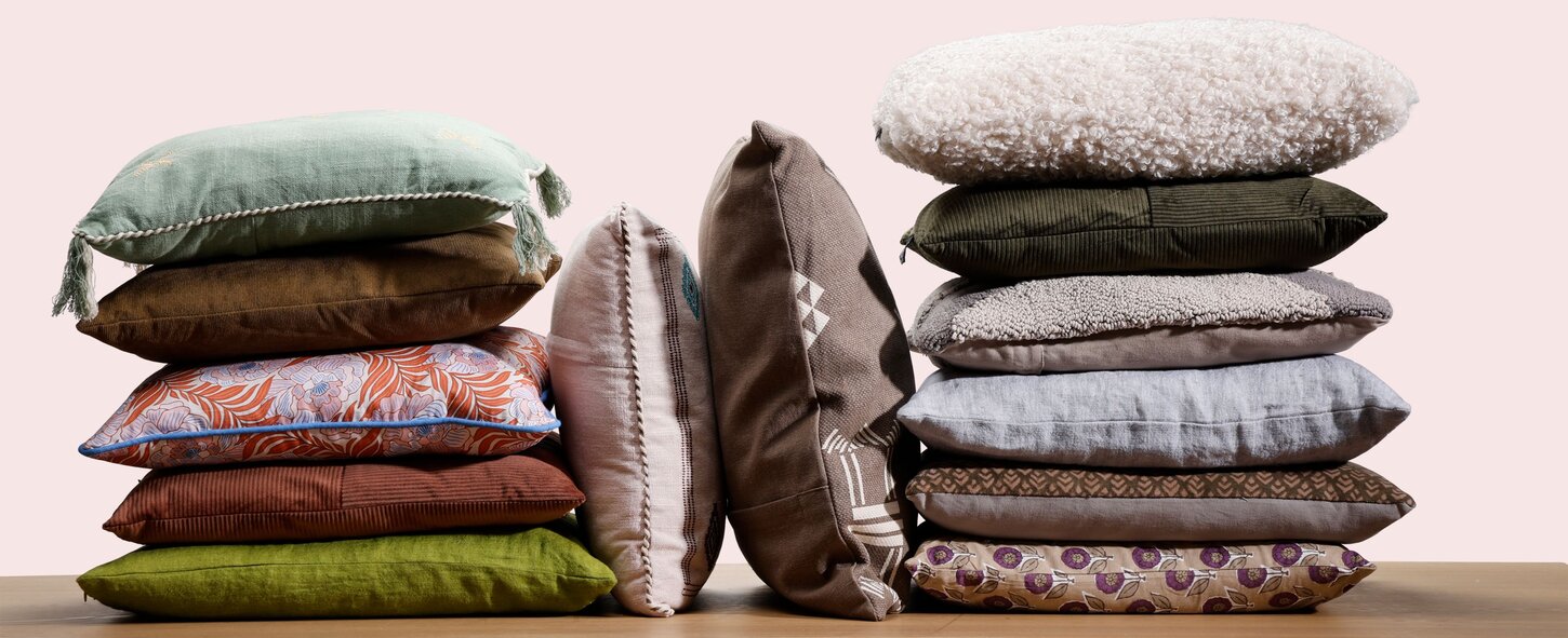 Mange forskellige slags pyntepuder stablet i bunker på en træbordplade