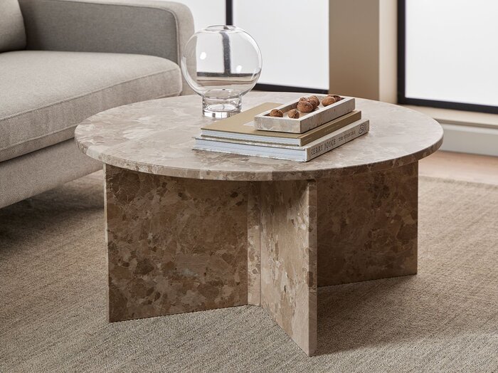 Rundt marmor sofabord i dagligstue indrettet med jordfarver.