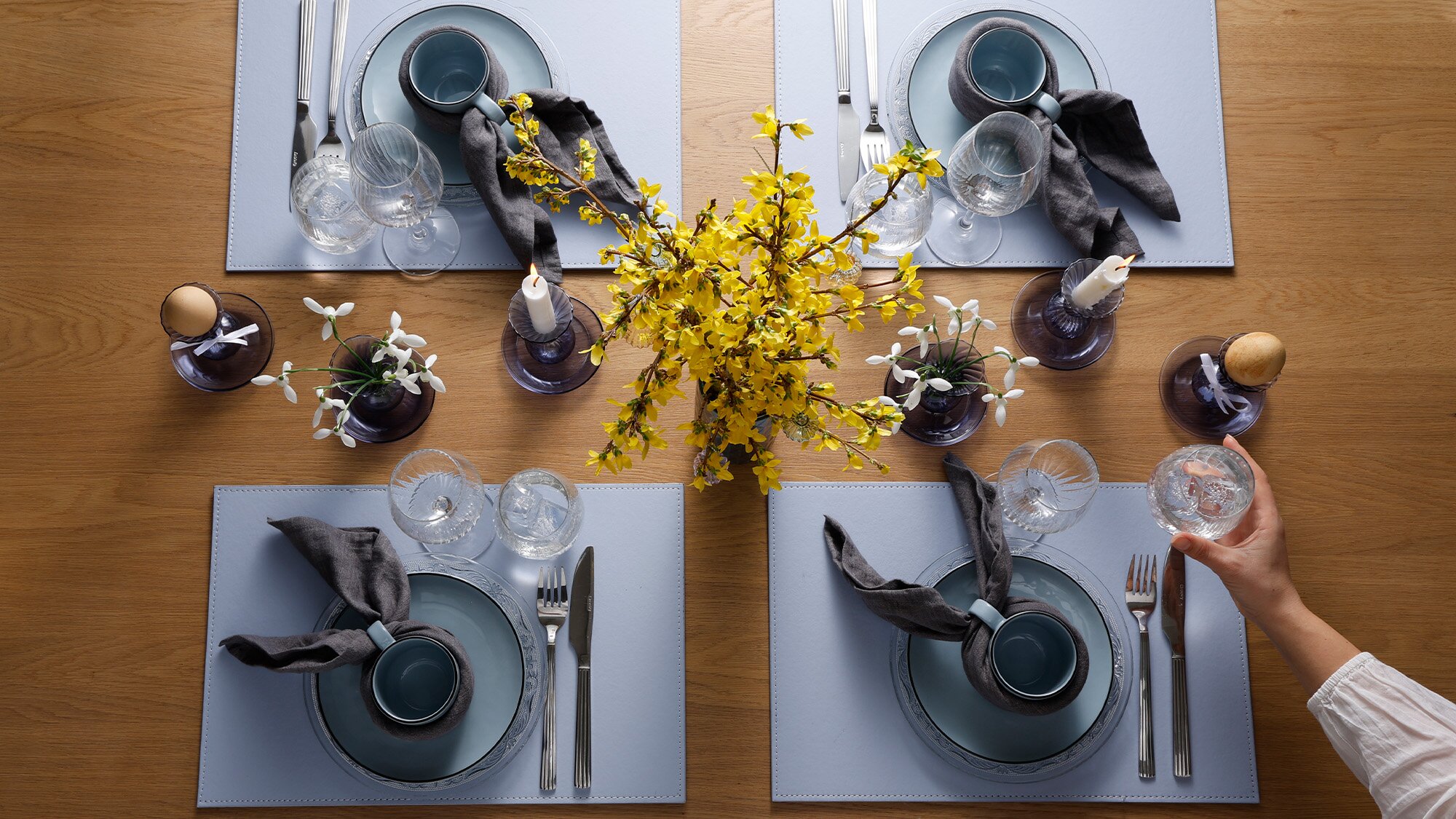 Påskebord dækket med blåt mandala stel, dækkeservietter, blomster og lys.