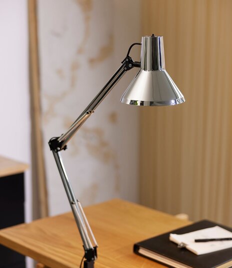 Krom arkitektlampe monteret på et træskrivebord.