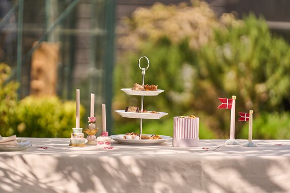 Havebord med lysestager, dannebrogs keramik flag, og små kager.