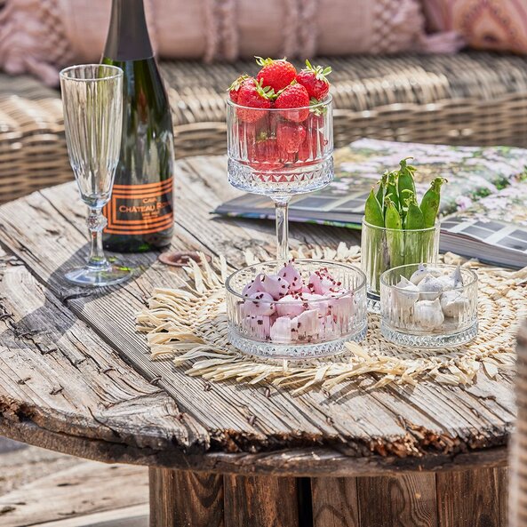 Sommerbord med champagne, samt glasskåle med elegant mønster fyldt med jordbær, ærter og skumfiduser.