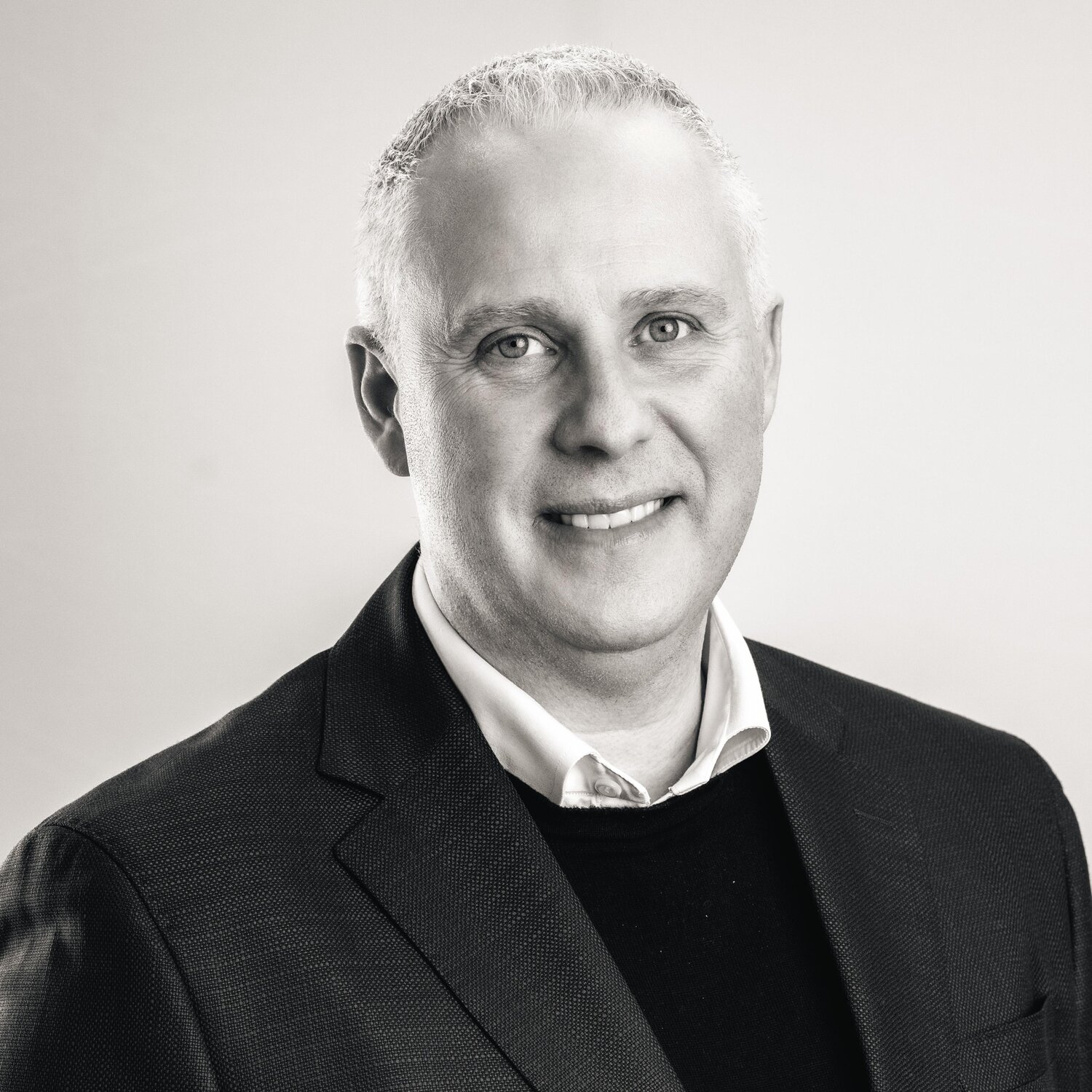 Sort-hvid portræt af Brian Seemann Broe iført blazer, skjorte og trøje, fotograferet mod en lys baggrund.