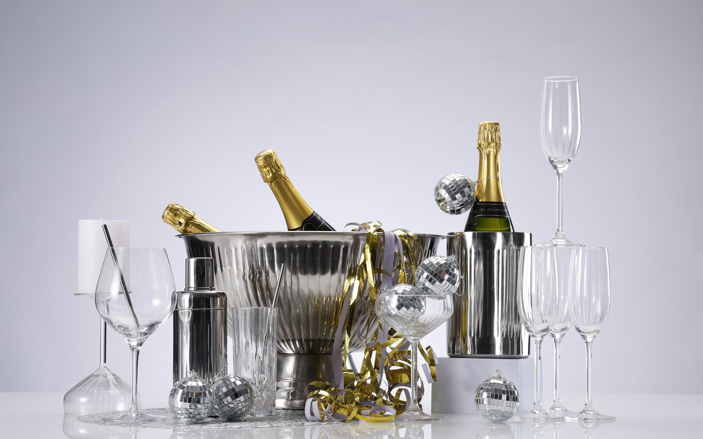 Nytårsstemning på et bord med champagneglas, vinkøler, champagnekøler, cocktail shaker, små diskokugler, terpentiner og drinksglas