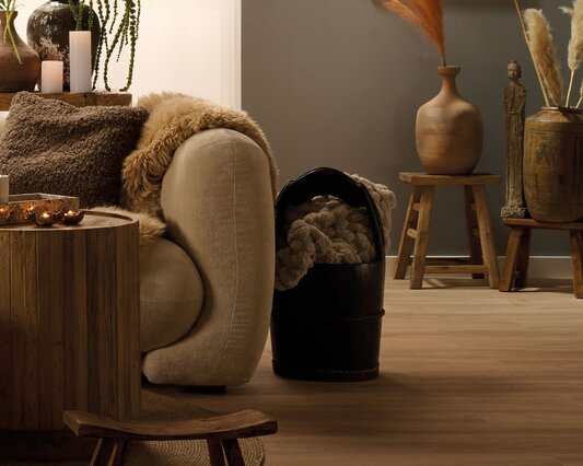 Hyggelig dagligstue indrettet i boho stil med en sofa, og en mørk rustik træspand ved siden af til at have plaider i.
