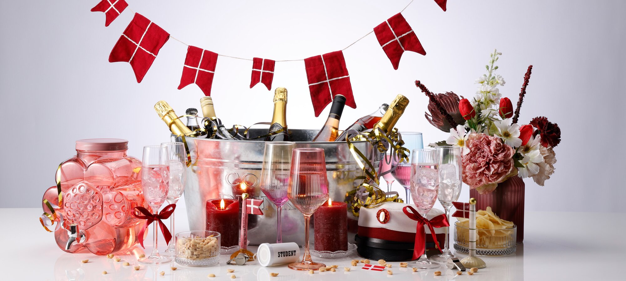 Rød studenterdækning med champagne, blomster og danske flag til festlig fejring