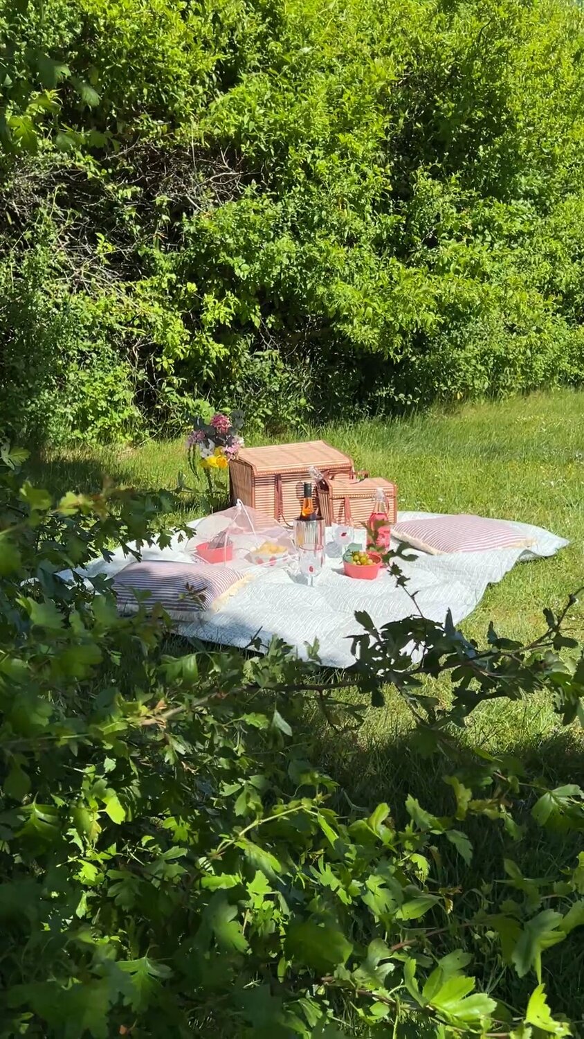 Mørkt rundt træsofabord med lysestager, blomster i vase, en skål med vindruer og to kopper kaffe. Bag bordet kan man se en beige sofa med puder i brun, pastel lilla og en rosa pude med frynser.