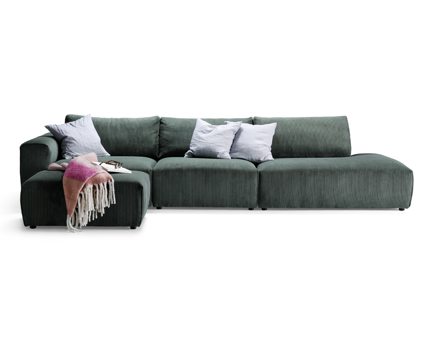 Grøn fløjl Monte Carlo modulsofa med modul med armlæn, modul uden armlæn og open end. Modulsofaen har en puf og er pyntet med lyseblå puder og lyserød plaid.