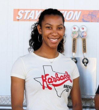 Woman standing in front of draft handles in a karbach t shirt