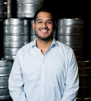 Man standing in front of a stack of metal beer barrels