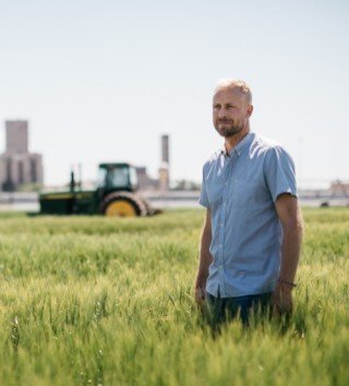 Man standing in a wheat field with a tractor in the background