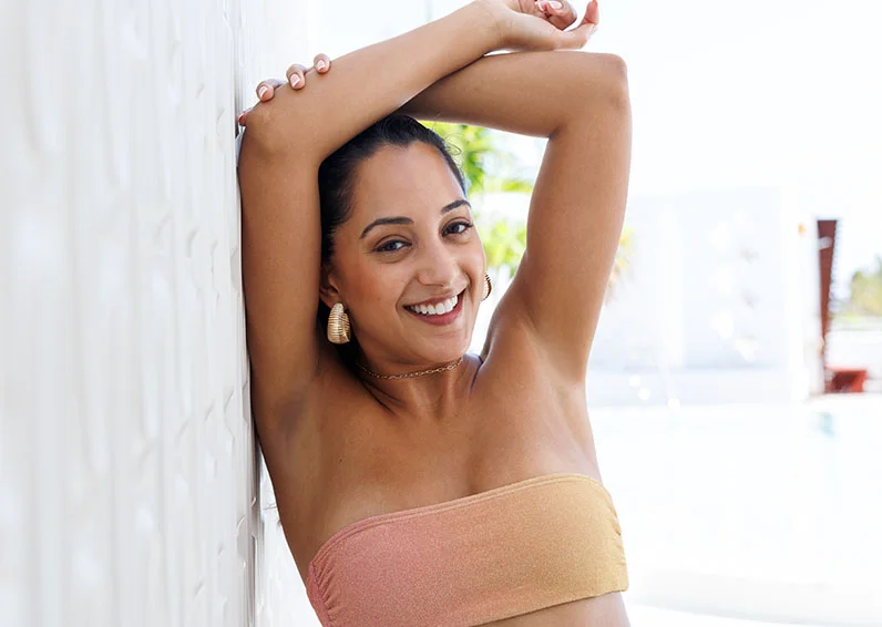 Woman leaning against a concrete wall with her arms above her head
