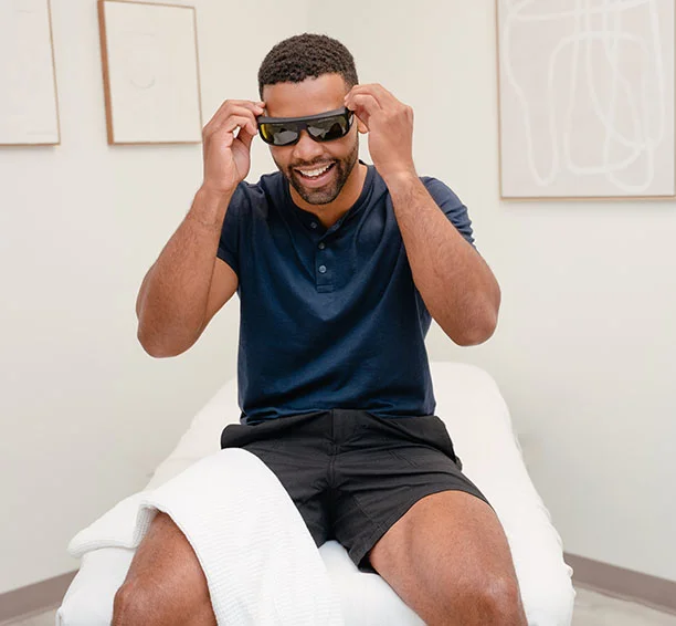 Smiling man sitting in a Milan treatment room in a blue shirt getting ready for his Men's Brazilian laser hair removal treatment